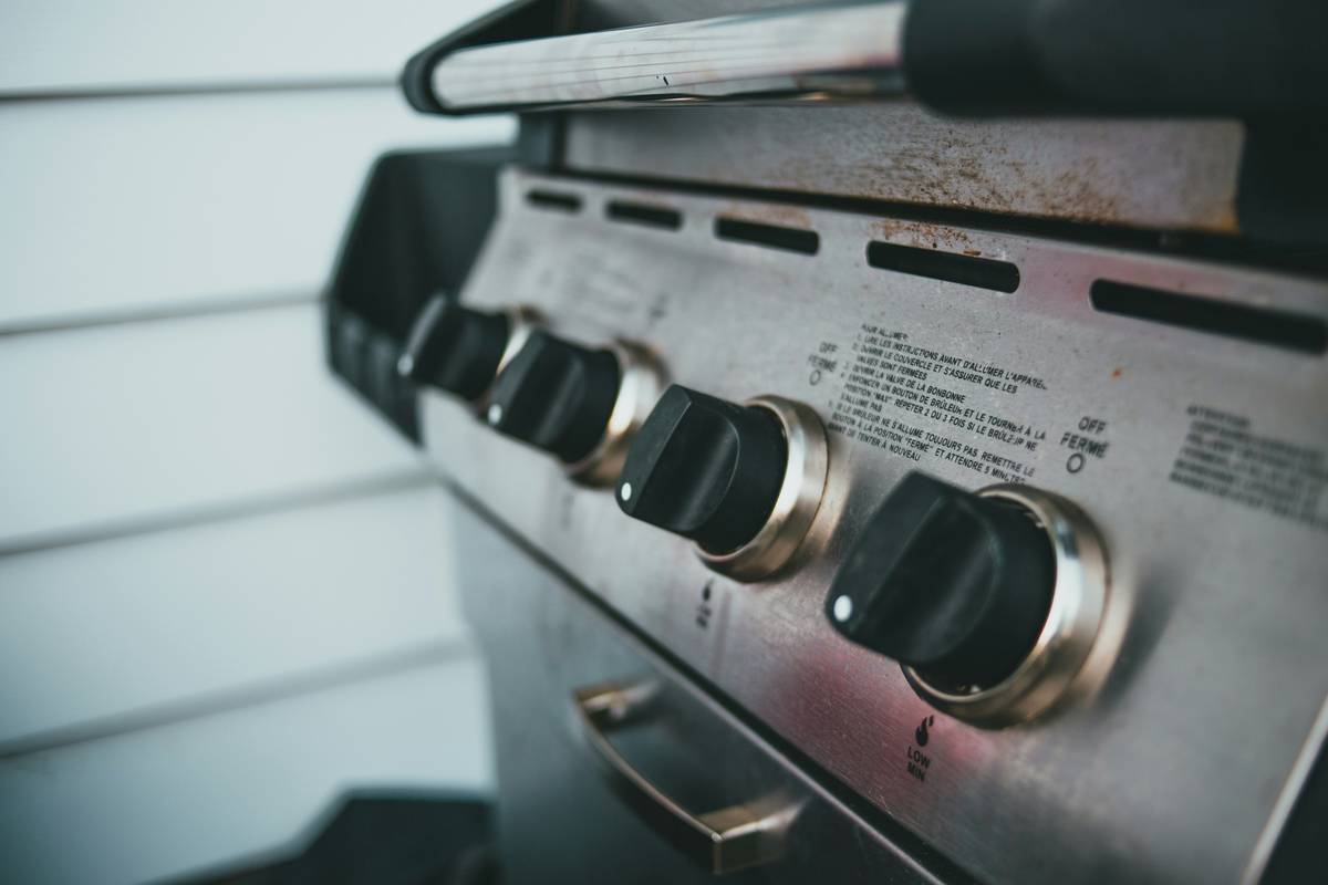 Close-up of a Klein electric grill control panel showing thermostat housing, multimeter probes measuring voltage across terminals, labeled 'temperature control thermostat electric maintenance klein'